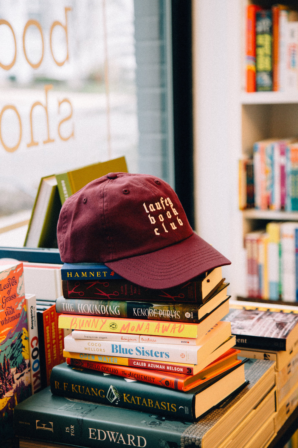 Maroon cap on a stack of books with bookshelf in the background