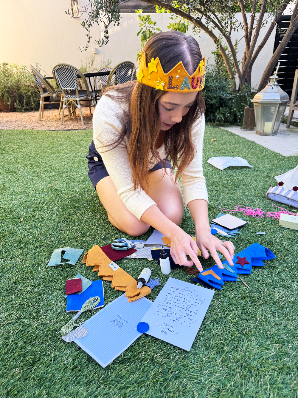 Person wearing a crown sitting on grass with craft materials