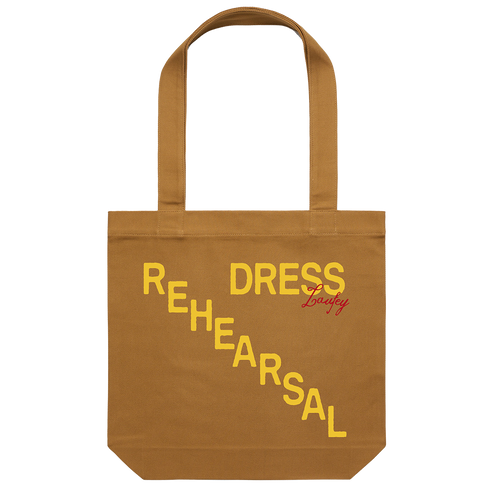 A camel-colored cotton tote bag with the words 'REHEARSAL' and 'DRESS' printed in a yellow gradient on the side.
