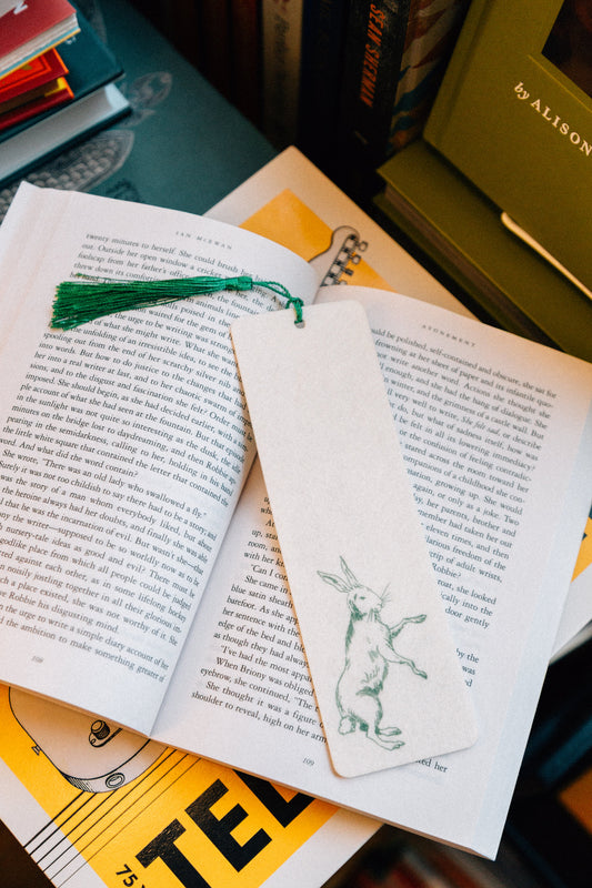 Open book with a decorative bookmark featuring a rabbit illustration, placed on top of other books.