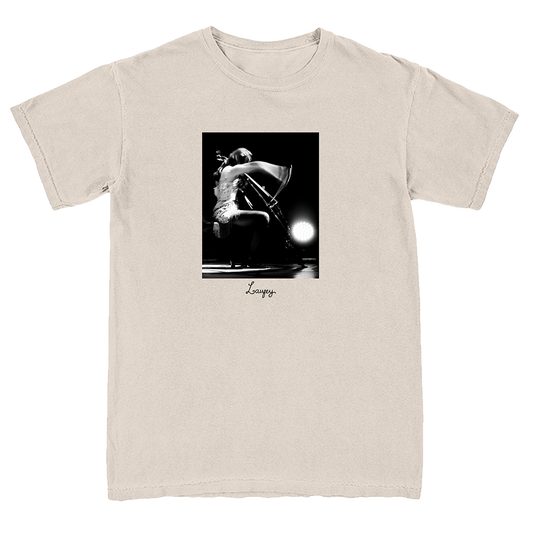 A light beige crewneck t-shirt featuring a black and white graphic print of a cellist on stage, with the name 'Loursy' printed in script below the image.