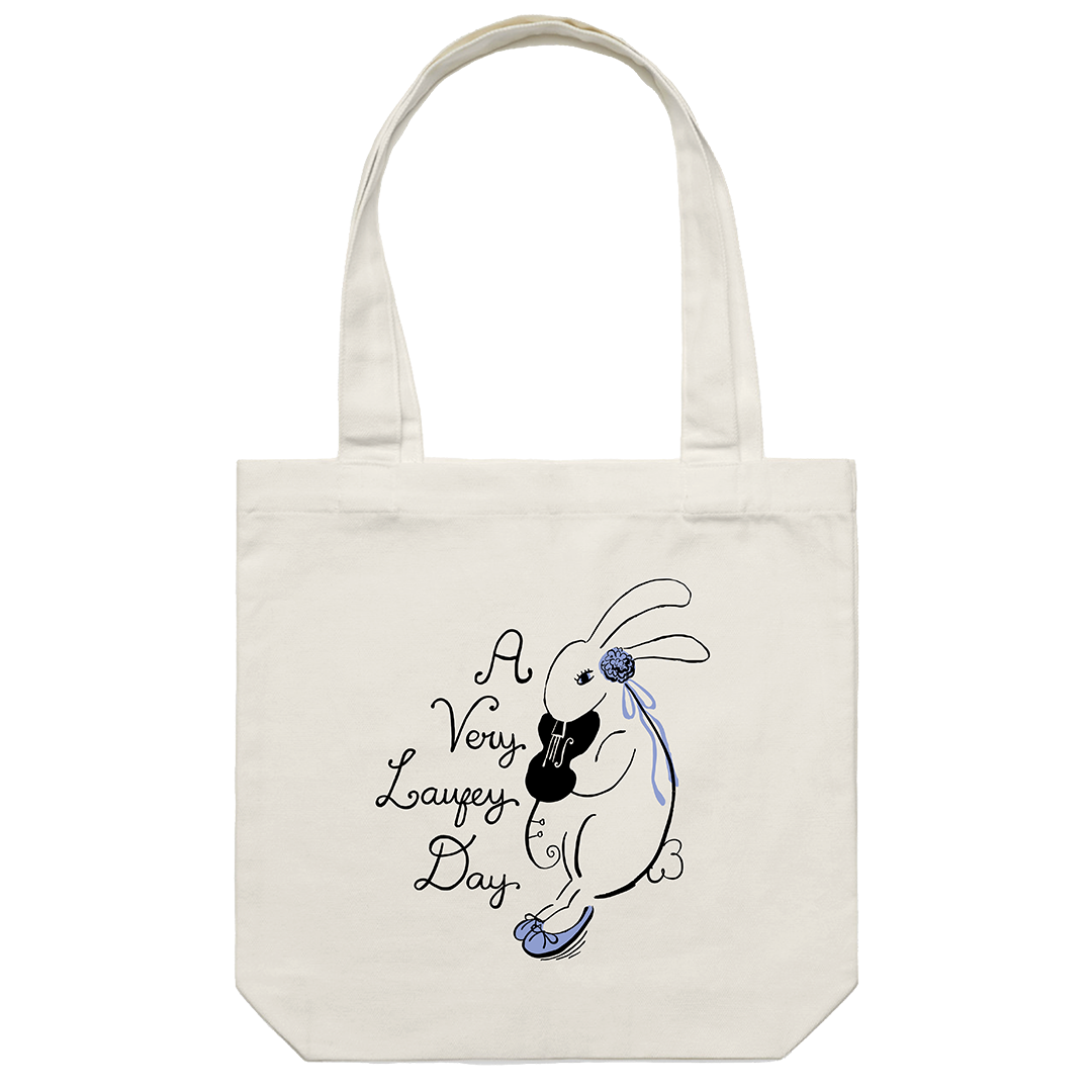An off-white canvas tote bag with two handles, featuring a black and blue line art illustration of a rabbit holding a guitar next to the text 'A Very Lafezy Day' on a plain white background.