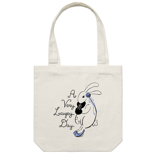 An off-white canvas tote bag with two handles, featuring a black and blue line art illustration of a rabbit holding a guitar next to the text 'A Very Lafezy Day' on a plain white background.