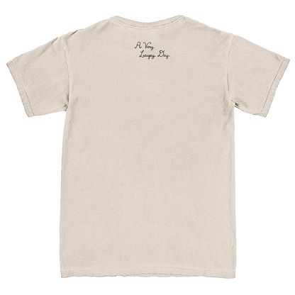 A light beige crewneck t-shirt shown from the back, featuring the text 'A Very Long Day' printed in a small black cursive font near the upper center back.