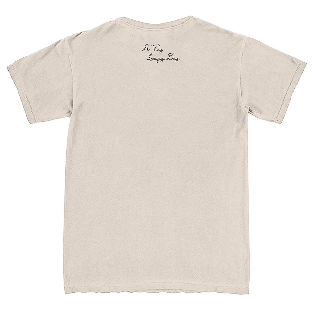 A light beige crewneck t-shirt shown from the back, featuring the text 'A Very Long Day' printed in a small black cursive font near the upper center back.